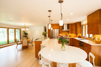 Open concept kitchen - mid-sized transitional l-shaped light wood floor open concept kitchen idea in Other with a double-bowl sink, shaker cabinets, medium tone wood cabinets, solid surface countertops, beige backsplash, stone tile backsplash, stainless steel appliances and an island