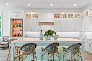 Mid-sized beach style l-shaped light wood floor, brown floor and tray ceiling kitchen photo in Other with white cabinets, quartz countertops, white backsplash, subway tile backsplash, paneled appliances, an island and white countertops