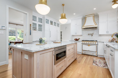 Large transitional l-shaped light wood floor and orange floor eat-in kitchen photo in Philadelphia with a farmhouse sink, recessed-panel cabinets, white cabinets, marble countertops, white backsplash, porcelain backsplash, paneled appliances, two islands and white countertops