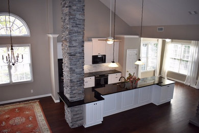Open concept kitchen - mid-sized traditional l-shaped medium tone wood floor and brown floor open concept kitchen idea in Atlanta with an undermount sink, raised-panel cabinets, white cabinets, solid surface countertops, an island and black countertops