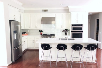 Kitchen - contemporary medium tone wood floor and brown floor kitchen idea in Los Angeles with an undermount sink, recessed-panel cabinets, white cabinets, quartz countertops, white backsplash, glass tile backsplash, stainless steel appliances and white countertops