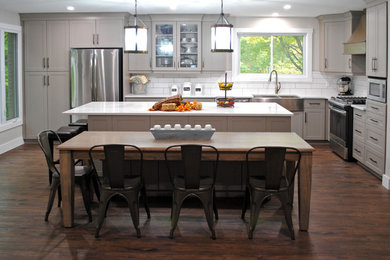 Inspiration for a mid-sized contemporary l-shaped medium tone wood floor and brown floor eat-in kitchen remodel in Other with a farmhouse sink, shaker cabinets, gray cabinets, quartzite countertops, white backsplash, subway tile backsplash, stainless steel appliances, an island and white countertops
