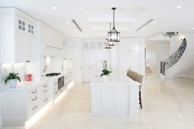 Photo of a traditional l-shaped eat-in kitchen in Sydney with a farmhouse sink, recessed-panel cabinets, white cabinets, marble benchtops, white splashback, marble splashback, black appliances, marble floors, with island, beige floor and white benchtop.