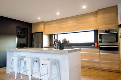 Inspiration for a mid-sized contemporary galley kitchen pantry in Hobart with a drop-in sink, louvered cabinets, light wood cabinets, concrete benchtops, black splashback, ceramic splashback, stainless steel appliances, light hardwood floors and with island.