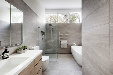 Design ideas for a large contemporary master bathroom in Sydney with a freestanding tub, a curbless shower, a one-piece toilet, gray tile, porcelain tile, white walls, porcelain floors, an undermount sink, engineered quartz benchtops, grey floor, a hinged shower door, white benchtops, flat-panel cabinets and light wood cabinets.