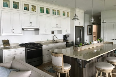 Example of a large beach style single-wall medium tone wood floor and brown floor eat-in kitchen design in New York with an undermount sink, shaker cabinets, gray cabinets, stainless steel appliances, an island, white backsplash, cement tile backsplash and beige countertops