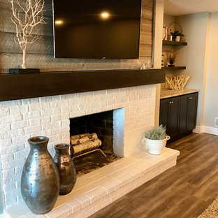 This is an example of a medium sized traditional look-out basement in Grand Rapids with beige walls, vinyl flooring, a standard fireplace, a brick fireplace surround and grey floors.