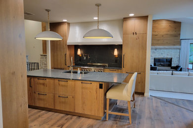 Example of a large transitional l-shaped medium tone wood floor, brown floor and vaulted ceiling kitchen pantry design in Denver with an undermount sink, beaded inset cabinets, medium tone wood cabinets, soapstone countertops, black backsplash, quartz backsplash, paneled appliances, an island and black countertops