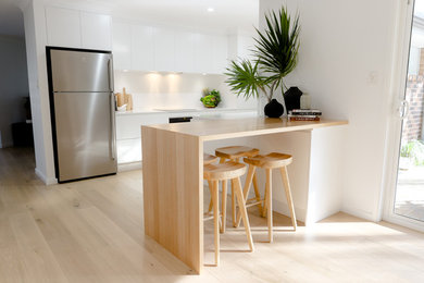 Design ideas for a mid-sized modern galley open plan kitchen in Central Coast with an undermount sink, flat-panel cabinets, white cabinets, quartz benchtops, white splashback, stone slab splashback, stainless steel appliances, light hardwood floors, with island, beige floor and white benchtop.