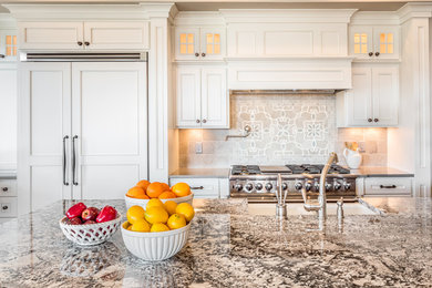 Example of a huge minimalist galley medium tone wood floor and brown floor eat-in kitchen design in Los Angeles with an undermount sink, white cabinets, granite countertops, beige backsplash, stone tile backsplash, stainless steel appliances, an island, raised-panel cabinets and multicolored countertops