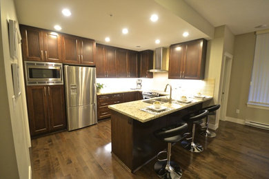 Kitchen - contemporary medium tone wood floor kitchen idea in Vancouver with a double-bowl sink, shaker cabinets, brown cabinets, granite countertops, beige backsplash, ceramic backsplash, stainless steel appliances and an island