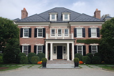 This is an example of a large traditional two-storey brick red house exterior in Other with a hip roof.