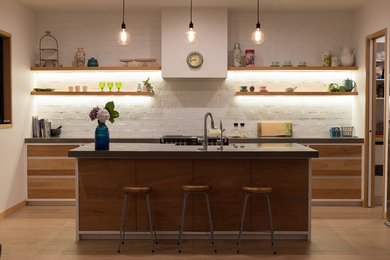 This is an example of a large contemporary galley kitchen in Other with a drop-in sink, medium wood cabinets, concrete benchtops, white splashback, brick splashback, stainless steel appliances, light hardwood floors, with island and brown floor.