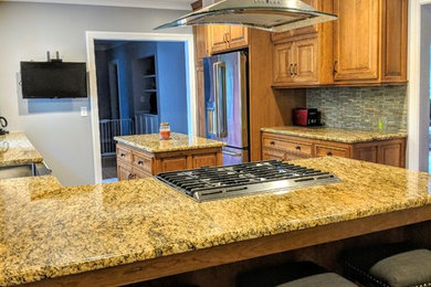 Kitchen - mid-sized transitional u-shaped porcelain tile and black floor kitchen idea in Other with a farmhouse sink, raised-panel cabinets, light wood cabinets, granite countertops, green backsplash, glass sheet backsplash, stainless steel appliances, an island and brown countertops