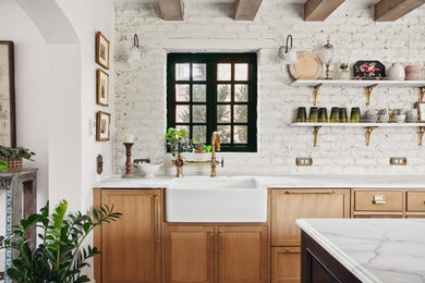 Mid-sized traditional single-wall eat-in kitchen in Denver with a farmhouse sink, flat-panel cabinets, light wood cabinets, granite benchtops, white splashback, brick splashback, black appliances, medium hardwood floors, with island, brown floor, white benchtop and exposed beam.