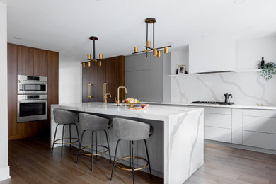 Large minimalist u-shaped medium tone wood floor and brown floor kitchen photo in Toronto with an undermount sink, flat-panel cabinets, gray cabinets, quartz countertops, white backsplash, quartz backsplash, stainless steel appliances, an island and white countertops