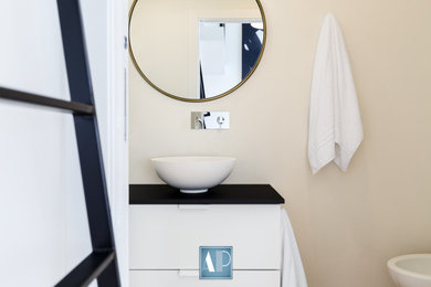Immagine di una piccola stanza da bagno design con ante bianche, WC sospeso, pareti beige, pavimento in legno verniciato, lavabo a bacinella, top in legno, pavimento marrone, top nero e mobile bagno sospeso