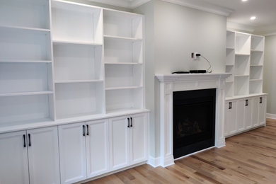 This is an example of a mid-sized contemporary open concept family room in Montreal with a library, grey walls, medium hardwood floors and a two-sided fireplace.