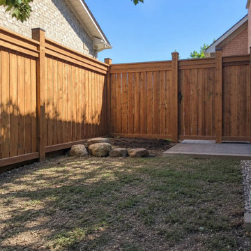 Pressure-treated wood fence with a matching gate and post caps beside a paver pa
