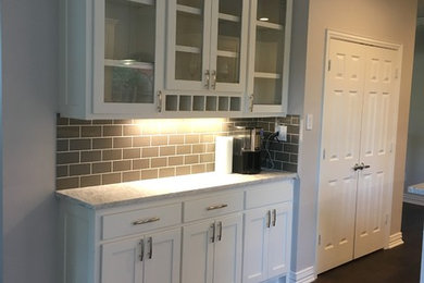 Small elegant single-wall dark wood floor and brown floor wet bar photo in Dallas with white cabinets, granite countertops, gray backsplash, glass tile backsplash and glass-front cabinets