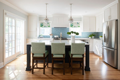 This is an example of a beach style l-shaped kitchen in Minneapolis with recessed-panel cabinets, white cabinets, blue splashback, stainless steel appliances, medium hardwood floors, with island, brown floor and white benchtop.