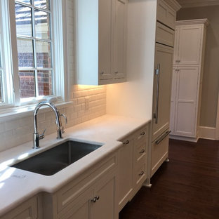 Inspiration pour une grande arrière-cuisine parallèle traditionnelle avec un évier encastré, un placard avec porte à panneau surélevé, des portes de placard blanches, un plan de travail en onyx, une crédence blanche, une crédence en carreau de céramique, un électroménager blanc, un sol en bois foncé, une péninsule, un sol marron et un plan de travail blanc.