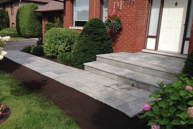 This is an example of a mid-sized transitional front yard verandah in Toronto with brick pavers.