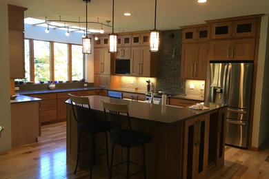 Example of a large trendy u-shaped light wood floor kitchen design in Other with shaker cabinets, light wood cabinets, quartz countertops, green backsplash, matchstick tile backsplash, stainless steel appliances and an island