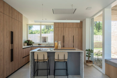 Moderne Küche in L-Form mit hellbraunen Holzschränken, Quarzit-Arbeitsplatte, Kücheninsel und grauer Arbeitsplatte in Sonstige