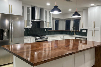 Inspiration for a 1950s l-shaped kitchen remodel in Dallas with an undermount sink, shaker cabinets, white cabinets, wood countertops, green backsplash, ceramic backsplash, stainless steel appliances, an island and white countertops