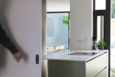 Exempel på ett mellanstort skandinaviskt vit vitt kök och matrum, med en integrerad diskho, släta luckor, grå skåp, bänkskiva i kvarts, vitt stänkskydd, integrerade vitvaror, ljust trägolv, en köksö och brunt golv