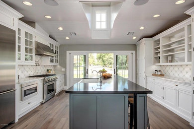 Inspiration for a mid-sized transitional galley light wood floor eat-in kitchen remodel in Phoenix with a farmhouse sink, white cabinets, quartz countertops, multicolored backsplash, porcelain backsplash, stainless steel appliances, an island and beaded inset cabinets