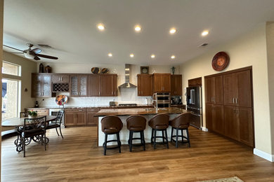 Large transitional vinyl floor and multicolored floor kitchen photo in Las Vegas with an undermount sink, shaker cabinets, medium tone wood cabinets, quartzite countertops, white backsplash, subway tile backsplash, stainless steel appliances, an island and multicolored countertops