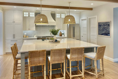 Kitchen - coastal light wood floor and exposed beam kitchen idea with a farmhouse sink, shaker cabinets, quartz countertops, blue backsplash and an island