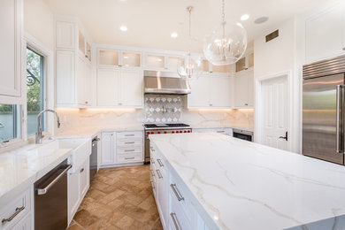 Example of a mid-sized transitional l-shaped porcelain tile and beige floor enclosed kitchen design in Orange County with a farmhouse sink, recessed-panel cabinets, white cabinets, quartz countertops, white backsplash, marble backsplash, stainless steel appliances and an island