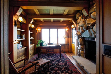 Example of a large mountain style freestanding desk medium tone wood floor study room design in Other with brown walls, a standard fireplace and a stone fireplace