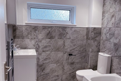 This is an example of a medium sized modern bathroom in London with a corner bath, a shower/bath combination, a two-piece toilet, grey tiles, porcelain tiles, a wall-mounted sink, a single sink and white walls.