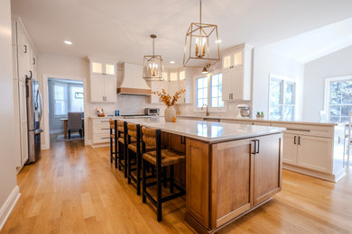 Example of a large transitional l-shaped light wood floor eat-in kitchen design in DC Metro with an undermount sink, shaker cabinets, white cabinets, quartz countertops, white backsplash, porcelain backsplash, stainless steel appliances, an island and white countertops