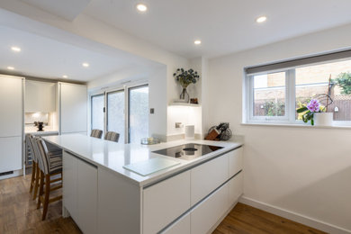 Small contemporary galley open plan kitchen in Sussex with flat-panel cabinets, white cabinets, quartzite benchtops, white splashback, engineered quartz splashback, a peninsula and white benchtop.