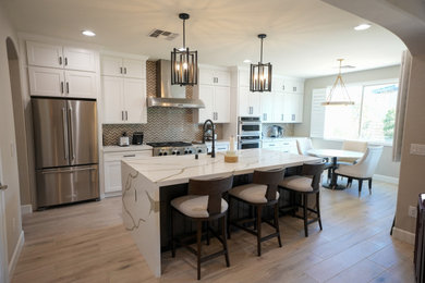 Eat-in kitchen - mid-sized modern galley brown floor and tray ceiling eat-in kitchen idea in Las Vegas with a farmhouse sink, shaker cabinets, white cabinets, quartz countertops, multicolored backsplash, stone tile backsplash, stainless steel appliances, an island and white countertops