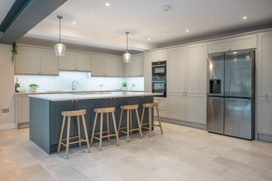 Design ideas for a large modern galley open plan kitchen in Hertfordshire with a built-in sink, shaker cabinets, grey cabinets, quartz worktops, white splashback, black appliances, an island and white worktops.