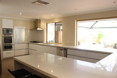Expansive modern u-shaped eat-in kitchen in Perth with a double-bowl sink, white cabinets, quartz benchtops, white splashback, stone slab splashback, stainless steel appliances and ceramic floors.