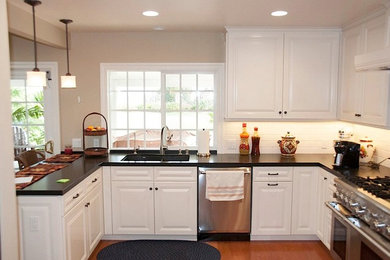 Example of a classic u-shaped eat-in kitchen design in Orange County with recessed-panel cabinets, white cabinets, granite countertops, white backsplash, stainless steel appliances and no island