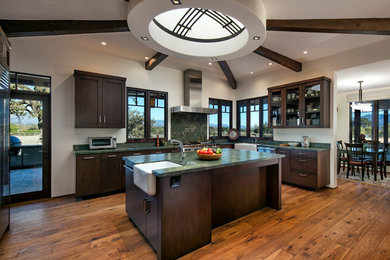 Inspiration for a large transitional eat-in kitchen in Santa Barbara with a farmhouse sink, flat-panel cabinets, dark wood cabinets, stainless steel appliances, medium hardwood floors, with island, granite benchtops, green splashback and stone slab splashback.