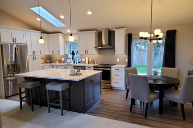 Example of a l-shaped laminate floor, brown floor and vaulted ceiling eat-in kitchen design in Seattle with an undermount sink, shaker cabinets, white cabinets, quartz countertops, gray backsplash, glass tile backsplash, stainless steel appliances, an island and multicolored countertops