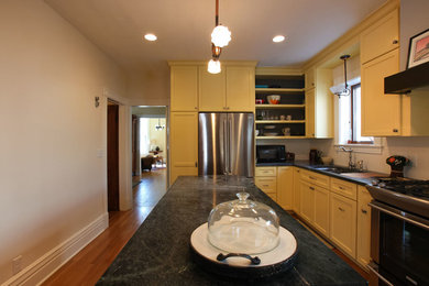 Elegant l-shaped enclosed kitchen photo in Minneapolis with an undermount sink, recessed-panel cabinets, yellow cabinets, soapstone countertops, white backsplash, mosaic tile backsplash and stainless steel appliances