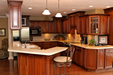 Inspiration for a large timeless medium tone wood floor eat-in kitchen remodel in Nashville with an integrated sink, raised-panel cabinets, medium tone wood cabinets, solid surface countertops, beige backsplash, porcelain backsplash, stainless steel appliances and an island
