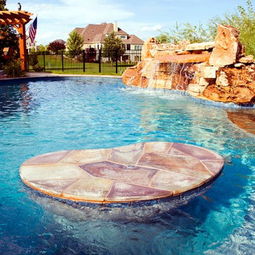 Free form pool with stone table, sun shelf, water feature, and outdoor kitchen,