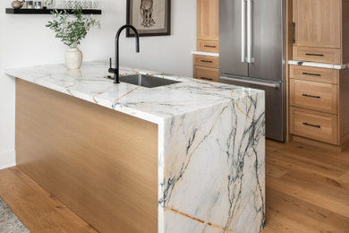 Small trendy medium tone wood floor and brown floor enclosed kitchen photo in New York with an undermount sink, shaker cabinets, brown cabinets, marble countertops, stainless steel appliances, an island and white countertops