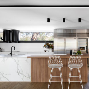 Design ideas for a large contemporary l-shaped kitchen pantry in Sydney with an undermount sink, flat-panel cabinets, solid surface benchtops, white splashback, black appliances, medium hardwood floors, with island and white benchtop.